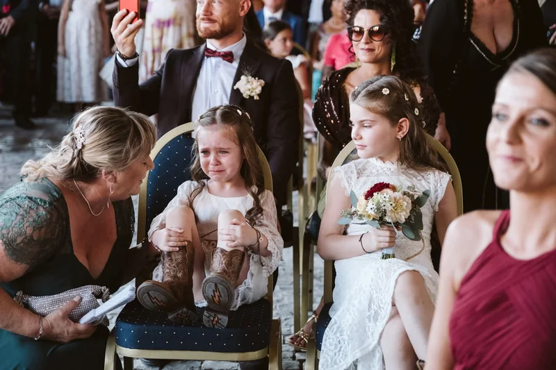 Due bambine in abito da cerimonia tra gli invitati, una viene confortata da una donna