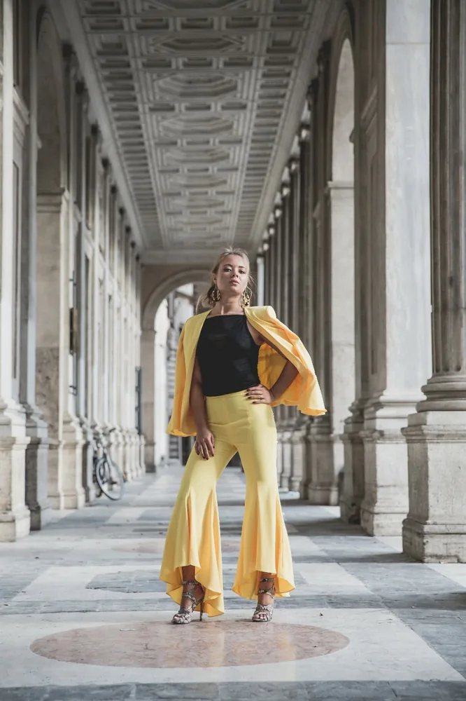 Modella in completo giallo sotto un porticato monumentale con colonne di pietra