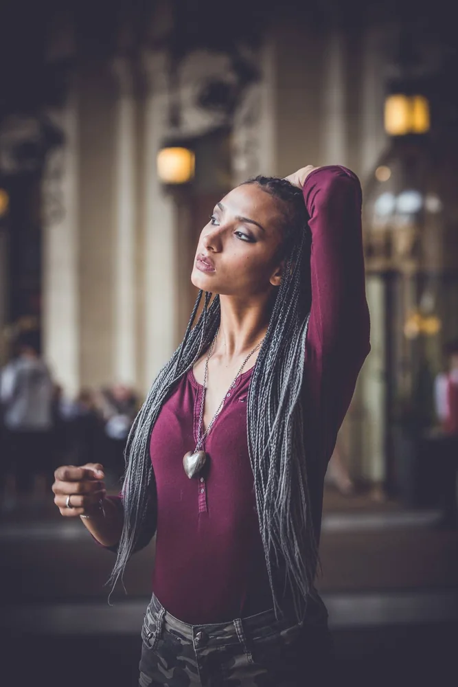 Modella con lunghe trecce e top bordeaux in un interno monumentale