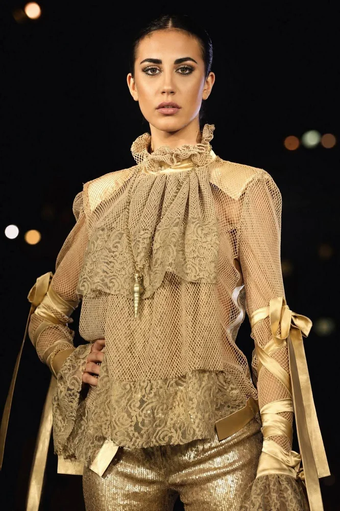 Modella in abito dorato con dettagli di rete, paillettes e fiocchi, su sfondo scuro