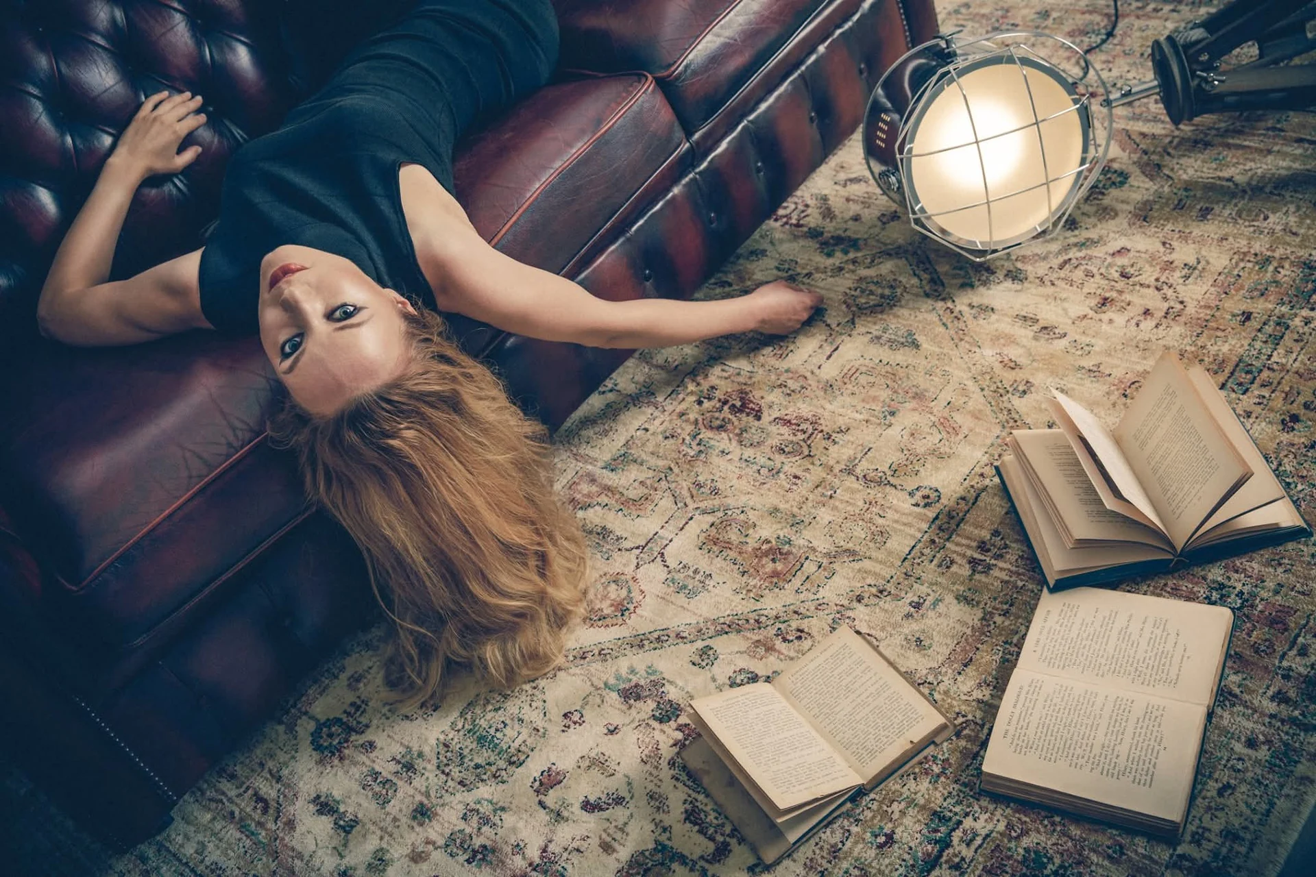 Scatto di moda su un divano in pelle, tra libri e luce di scena