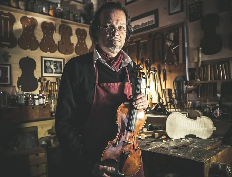 Ritratto di un artigiano con un violino nella sua bottega, tra strumenti e tavoli da lavoro