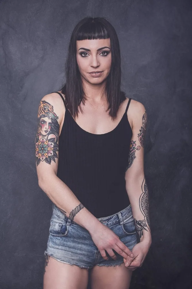 Ritratto in studio di una donna con frangia corta, canotta nera e braccia tatuate