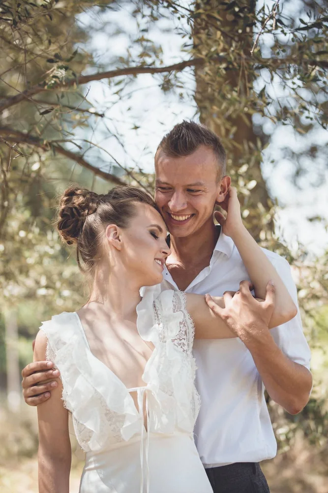 Coppia in abiti da sposi si abbraccia sorridendo tra i rami degli alberi