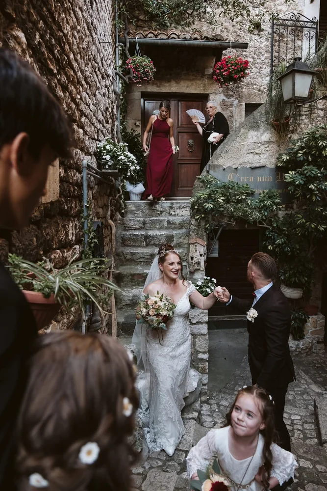 Sposi si tengono per mano lungo una scalinata di un borgo tra gli invitati