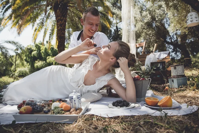 Coppia in abiti da sposi durante un picnic tra frutta, libri e luce naturale