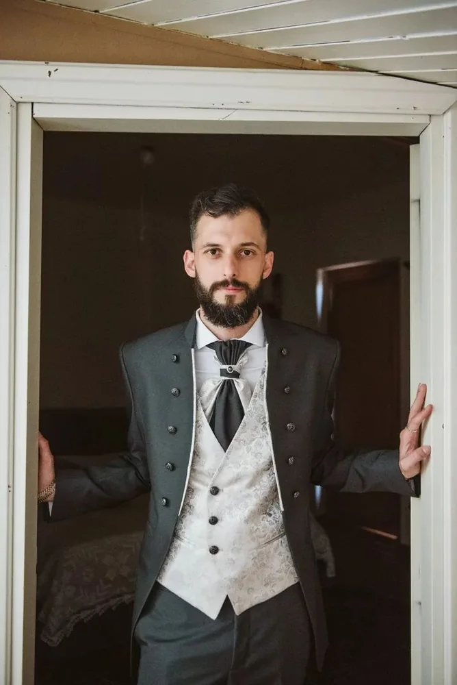 Sposo con barba e abito da cerimonia affacciato alla cornice di una porta